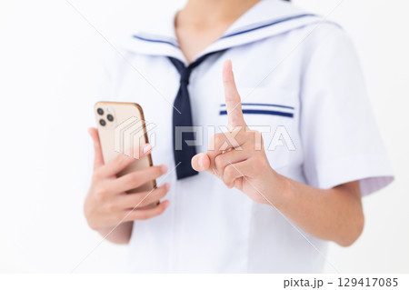 スマホを持って人差し指を立てる夏の学生服姿の中学生女子 129417085
