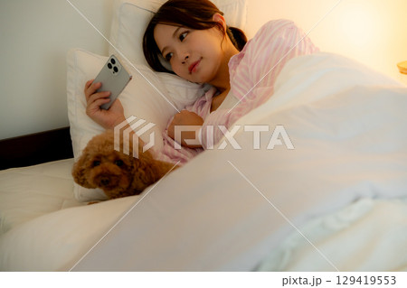 ベッドの中でスマホを操作する若い女性 ベッドの中でスマホを操作する若い女性 129419553