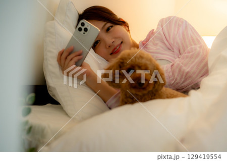 ベッドの中でスマホを操作する若い女性 ベッドの中でスマホを操作する若い女性 129419554