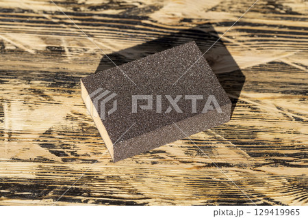 hard sandpaper on sponge for manual polishing of wooden surfaces, wooden board made of pine planks for polishing with sandpaper on the construction site 129419965