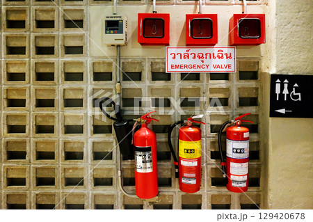 Emergency valves in Thai characters on a white sign with red fire extinguisher and toilet label on concrete wall 129420678