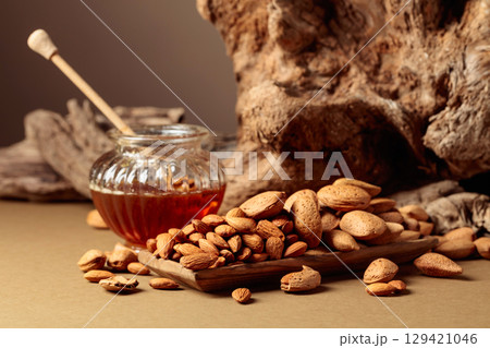 Almond nuts in a wooden dish and honey in a glass jar. Almond nuts in a wooden dish and honey in a glass jar. 129421046