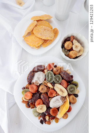 Mix of dried tropical fruits, nuts, and raisins on a white table. Mix of dried tropical fruits, nuts, and raisins on a white table. 129421203