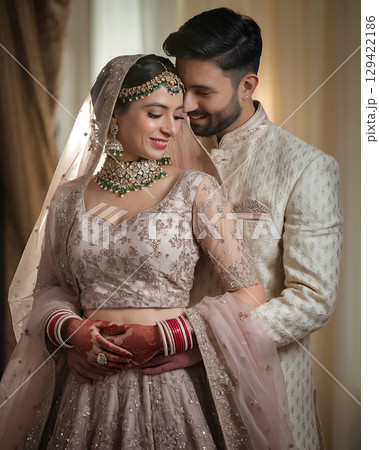 Indian Wedding Couple in Traditional Embroidered Attire Sharing Intimate Moment with Ornate Jewelry Indian Wedding Couple in Traditional Embroidered Attire Sharing Intimate Moment with Ornate Jewelry 129422186