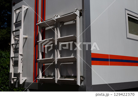 Close up of side of emergency rescue vehicle showing mounted ladder and storage racks. The bright orange and blue stripes, along with functional design, emphasize its role in emergency operations 129422370