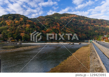 Picturesque view of Katsura River in Kyoto, Japan, bordered by walkway framed by forested mountains 129423091