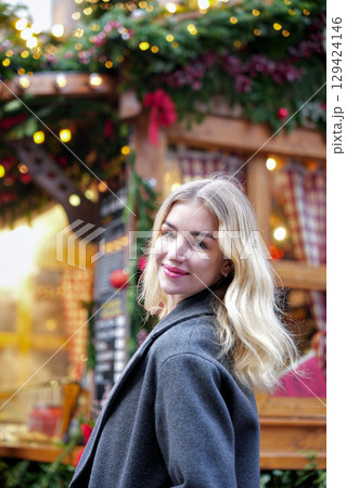 Blonde woman smiling at Christmas market in festive city lights 129424146