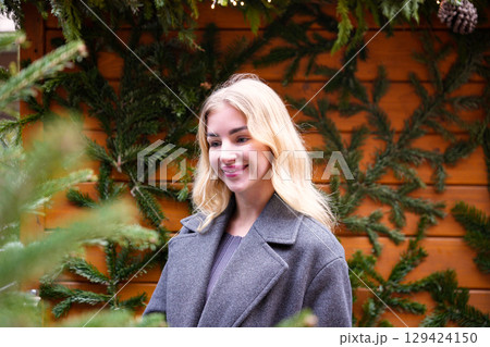 Blonde woman smiling near decorated Christmas tree at holiday market 129424150