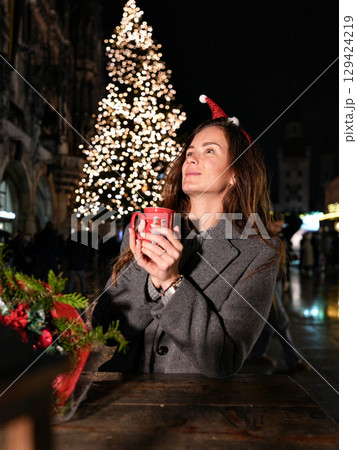 Munich Christmas market woman holding hot drink by festive tree 129424219
