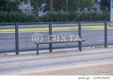 Empty modern bus stop shelter featuring a long wooden bench on a quiet city street, symbolizing urban public transportation and waiting 129424683