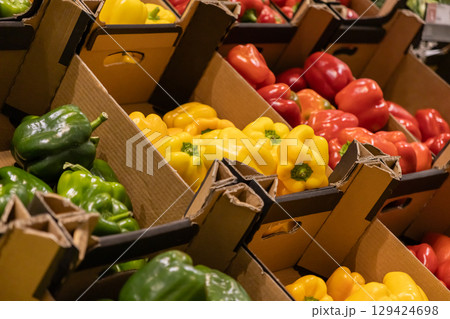 Colorful bell peppers of green, yellow, and red colors arranged neatly in cardboard boxes at a supermarket for fresh produce display 129424698