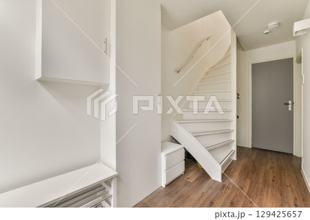 A sleek and bright hallway featuring modern architecture, clean lines, and minimalist decor. The well-lit space has a stylish staircase and functional storage units. 129425657