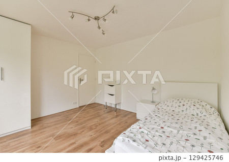 A clean and minimalistic bedroom featuring white walls, wooden flooring, and simple decor elements. The design promotes a sense of tranquility and simplicity. 129425746