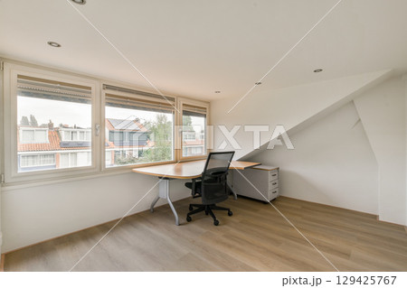 A minimalist office space featuring a desk and chair beside large windows that provide a view of the cityscape outside. 129425767