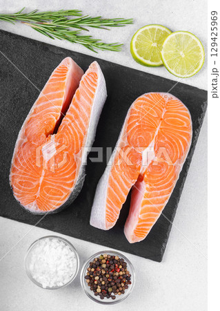 Fresh raw salmon or trout steaks with tomatoes, spices, rosemary and lime on white stone background 129425969