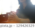 A Christian woman praying and worshipping with her hands clasped in meditation, with a church background featuring the Holy Cross of Jesus Christ. 129426329
