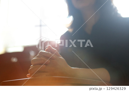 A Christian woman praying and worshipping with her hands clasped in meditation, with a church background featuring the Holy Cross of Jesus Christ. 129426329