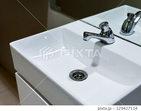 Modern white ceramic sink with chrome faucet in minimalist bathroom setting Modern white ceramic sink with chrome faucet in minimalist bathroom setting 129427114