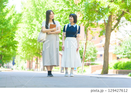 　緑あふれるキャンパスで談笑する学生2人 129427612