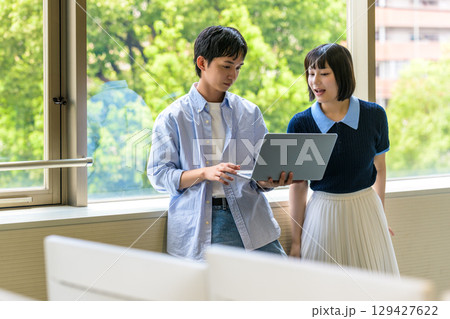 　ノートPCを抱え女性と立つ男子学生 129427622