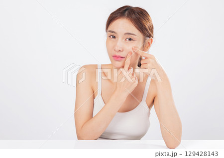 Acne appears around her forehead while acne near her nose adds to the concern, as she carefully squeezes spots and addresses skin care with honesty and self-awareness. isolated studio white background 129428143
