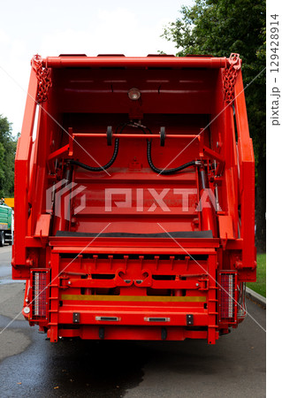 Back view of red garbage truck with hydraulic mechanism, control levers, and metal components. Industrial vehicle for waste management and city sanitation. Focus on truck rear and details 129428914