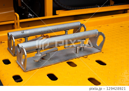 Close-up of wheel chocks on yellow tow truck platform, used to secure a car during towing. Metal brackets with springs ensure stability and prevent movement of vehicle during transportation 129428921