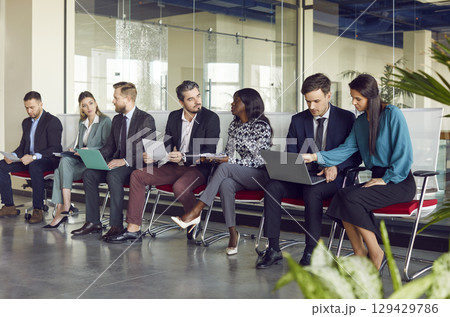 Diverse group of business people sitting in row collaborating and communicating during work meeting. Diverse group of business people sitting in row collaborating and communicating during work meeting. 129429786