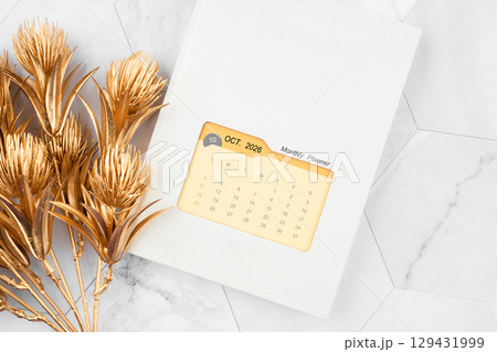 October 2026 calendar on monthly planner book with golden flower on white marble background. 129431999