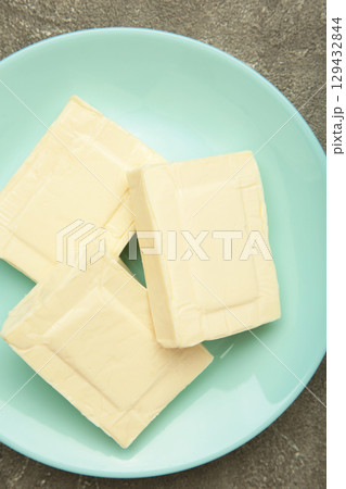 Processed cheese in foil on plate on grey concrete background Processed cheese in foil on plate on grey concrete background 129432844