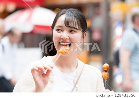 屋外で串カツ（串揚げ）を食べる女性｜大阪府大阪市道頓堀にて 129433350