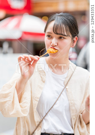 屋外で串カツ（串揚げ）を食べる女性｜大阪府大阪市道頓堀にて 129433351