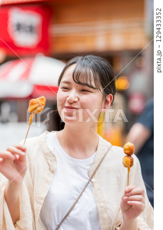屋外で串カツ（串揚げ）を食べる女性｜大阪府大阪市道頓堀にて 129433352