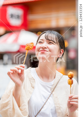屋外で串カツ(串揚げ)を食べる女性|大阪府大阪市道頓堀にて 屋外で串カツ(串揚げ)を食べる女性|大阪府大阪市道頓堀にて 129433354