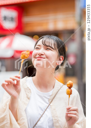 屋外で串カツ（串揚げ）を食べる女性｜大阪府大阪市道頓堀にて 129433355