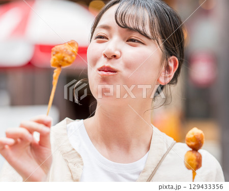 屋外で串カツ（串揚げ）を食べる女性｜大阪府大阪市道頓堀にて 129433356