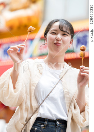 屋外で串カツ（串揚げ）を食べる女性｜大阪府大阪市道頓堀にて 129433359