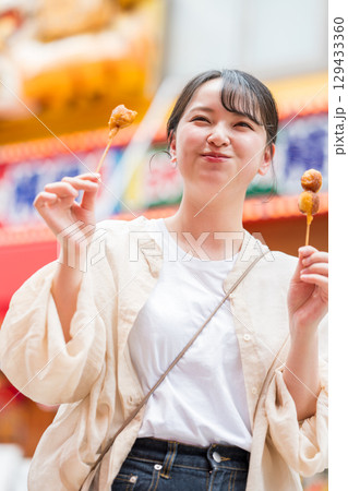 屋外で串カツ（串揚げ）を食べる女性｜大阪府大阪市道頓堀にて 129433360