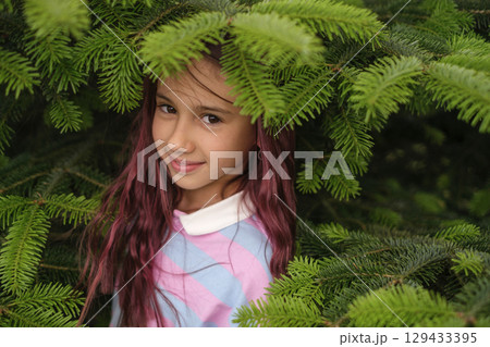 Portrait of a beautiful sweet girl among the branches of a green fir tree 129433395