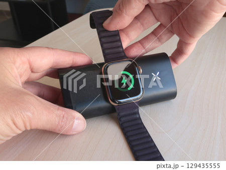 Woman charges her smart watch using portable wireless charger in room. Modern lifestyle, mobile technology, travel. Woman charges her smart watch using portable wireless charger in room. Modern lifestyle, mobile technology, travel. 129435555