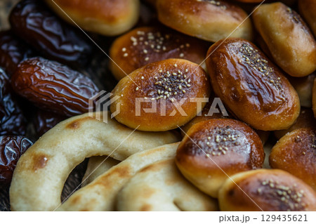 A rustic wooden plate holds a delicious arrangement of glossy dates and golden-brown pastries. The scene is illuminated by soft, crescent moon-shaped lights. A rustic wooden plate holds a delicious arrangement of glossy dates and golden-brown pastries. The scene is illuminated by soft, crescent moon-shaped lights. 129435621