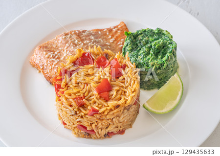 Elegant plated salmon with rice pilaf and creamy spinach on white round plate 129435633