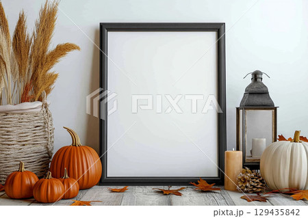 A blank, vertical black picture frame is a centerpiece surrounded by autumn decor. The decorations include pumpkins, lanterns with candles, dried leaves, and tall grasses. A blank, vertical black picture frame is a centerpiece surrounded by autumn decor. The decorations include pumpkins, lanterns with candles, dried leaves, and tall grasses. 129435842