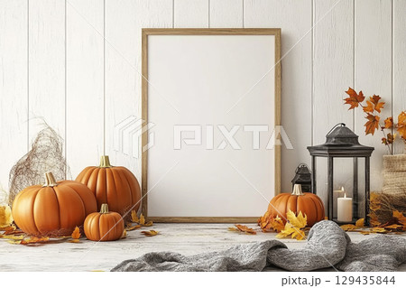 A blank, vertical black picture frame is a centerpiece surrounded by autumn decor. The decorations include pumpkins, lanterns with candles, dried leaves, and tall grasses. 129435844