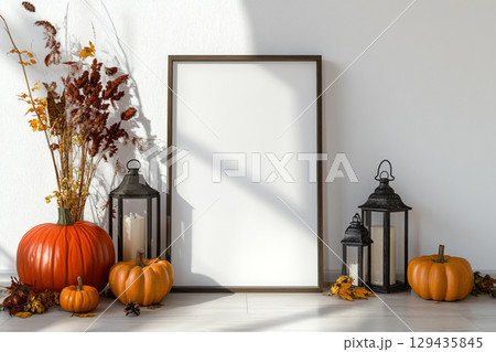 A blank, vertical black picture frame is a centerpiece surrounded by autumn decor. The decorations include pumpkins, lanterns with candles, dried leaves, and tall grasses. 129435845