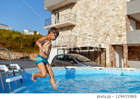 Boy jumping into outdoor swimming pool in summer Boy jumping into outdoor swimming pool in summer 129435969