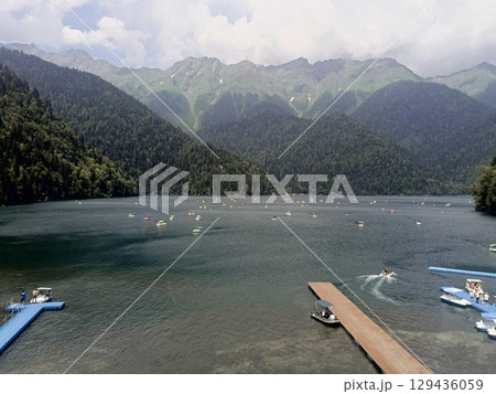 A vibrant recreational lake scene with people enjoying paddle boats, in a joyful mood, representing summer activities and tourism against a mountain backdrop 129436059