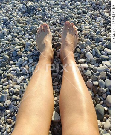 A woman's tanned legs with a carefree mood resting on a pebble beach background representing summer vacation and relaxation A woman's tanned legs with a carefree mood resting on a pebble beach background representing summer vacation and relaxation 129437167