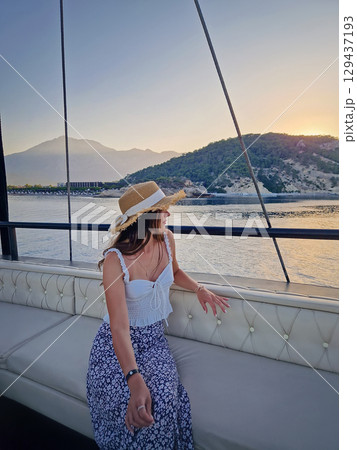 Young woman tourist wearing straw hat, sailing on a boat gazing out the Kiris resort coastline in Turkey. Female enjoying the views as cruising on the deep blue Mediterranean Sea 129437193