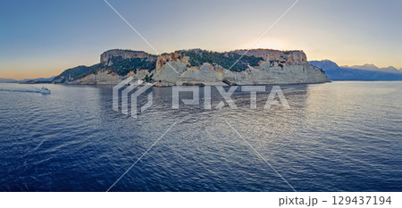 Evening seascape panorama with a boat cruising away on the blue sea, near the Pirate Cave in Kemer at sunset. Beautiful Turkish mediterranean coastline lined with tree covered rocky cliffs at dusk Evening seascape panorama with a boat cruising away on the blue sea, near the Pirate Cave in Kemer at sunset. Beautiful Turkish mediterranean coastline lined with tree covered rocky cliffs at dusk 129437194